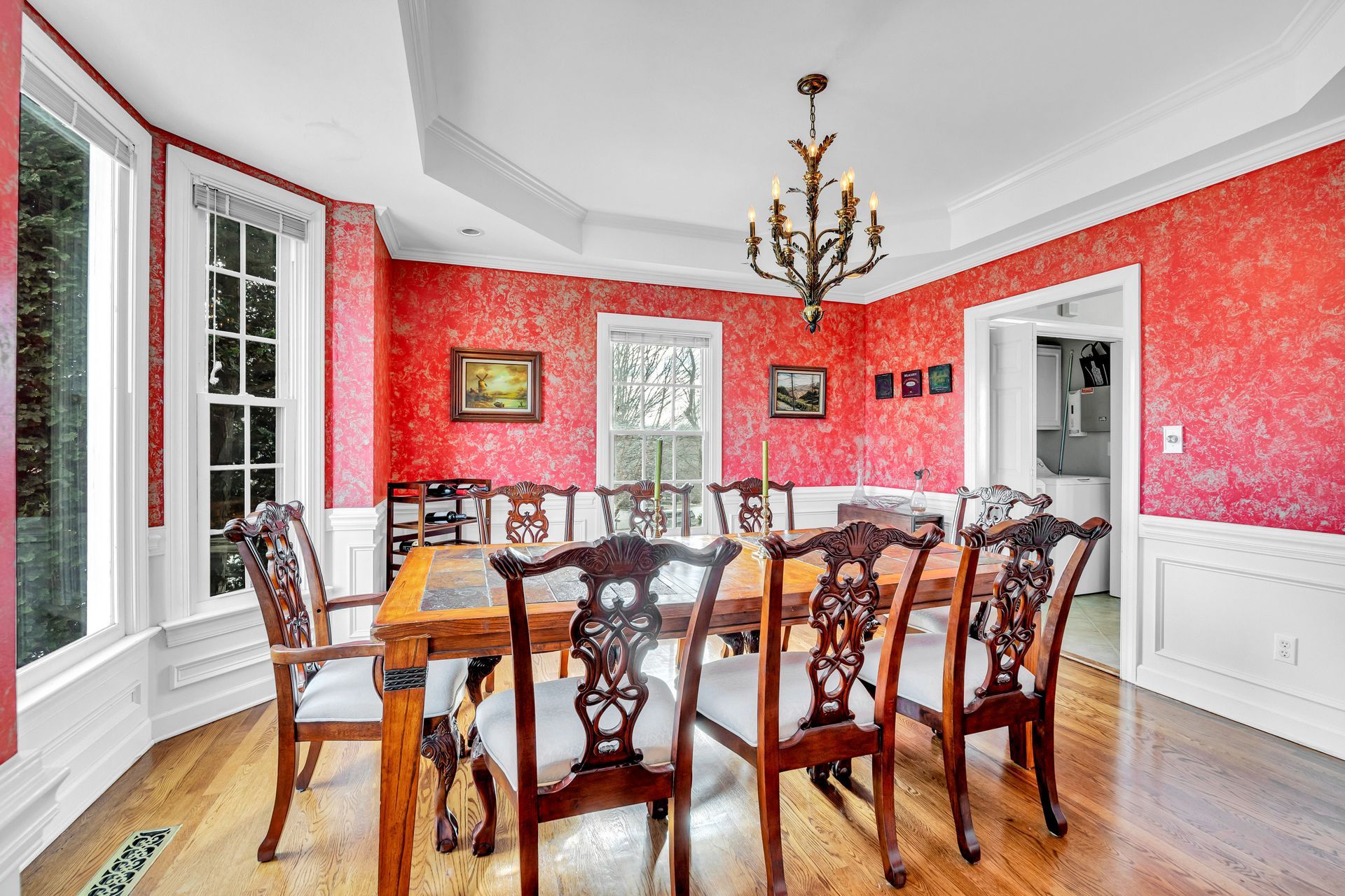Dining room with red patterned walls, wooden table and chairs, chandelier, and hardwood floors
