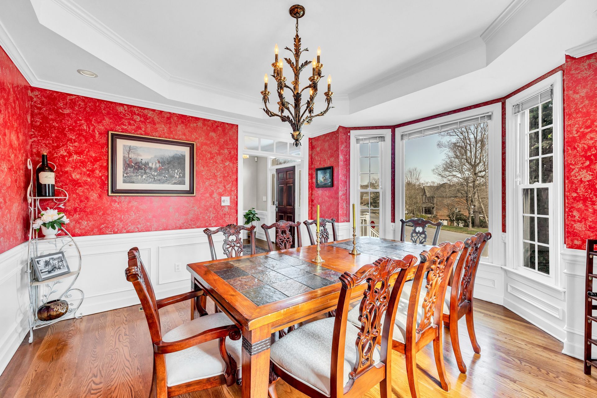 Elegant dining room with red walls, wood table, chandelier, and large bay windows