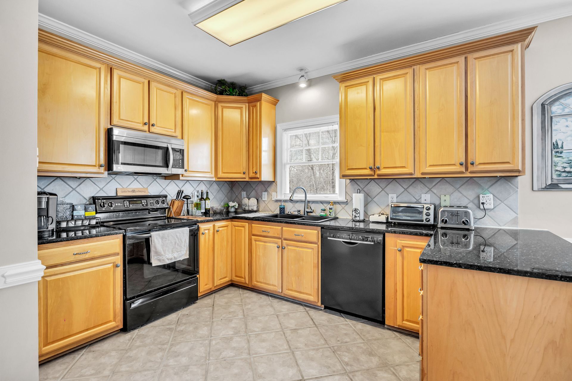 Bright kitchen with oak cabinets, black appliances, and a tiled floor around a central window.