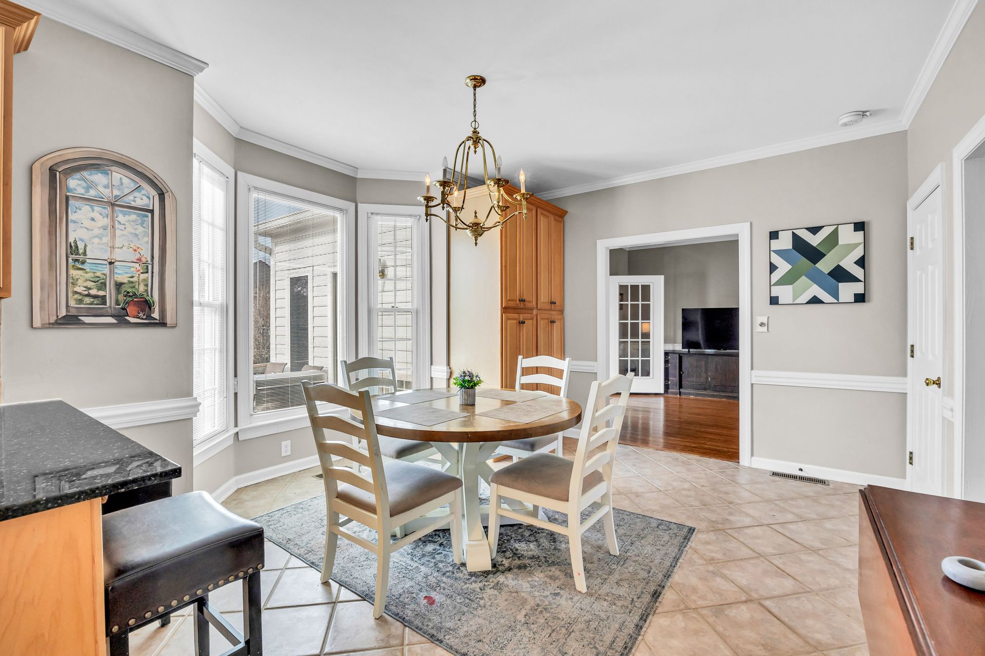Bright dining room with round table, chairs, chandelier, and large windows.