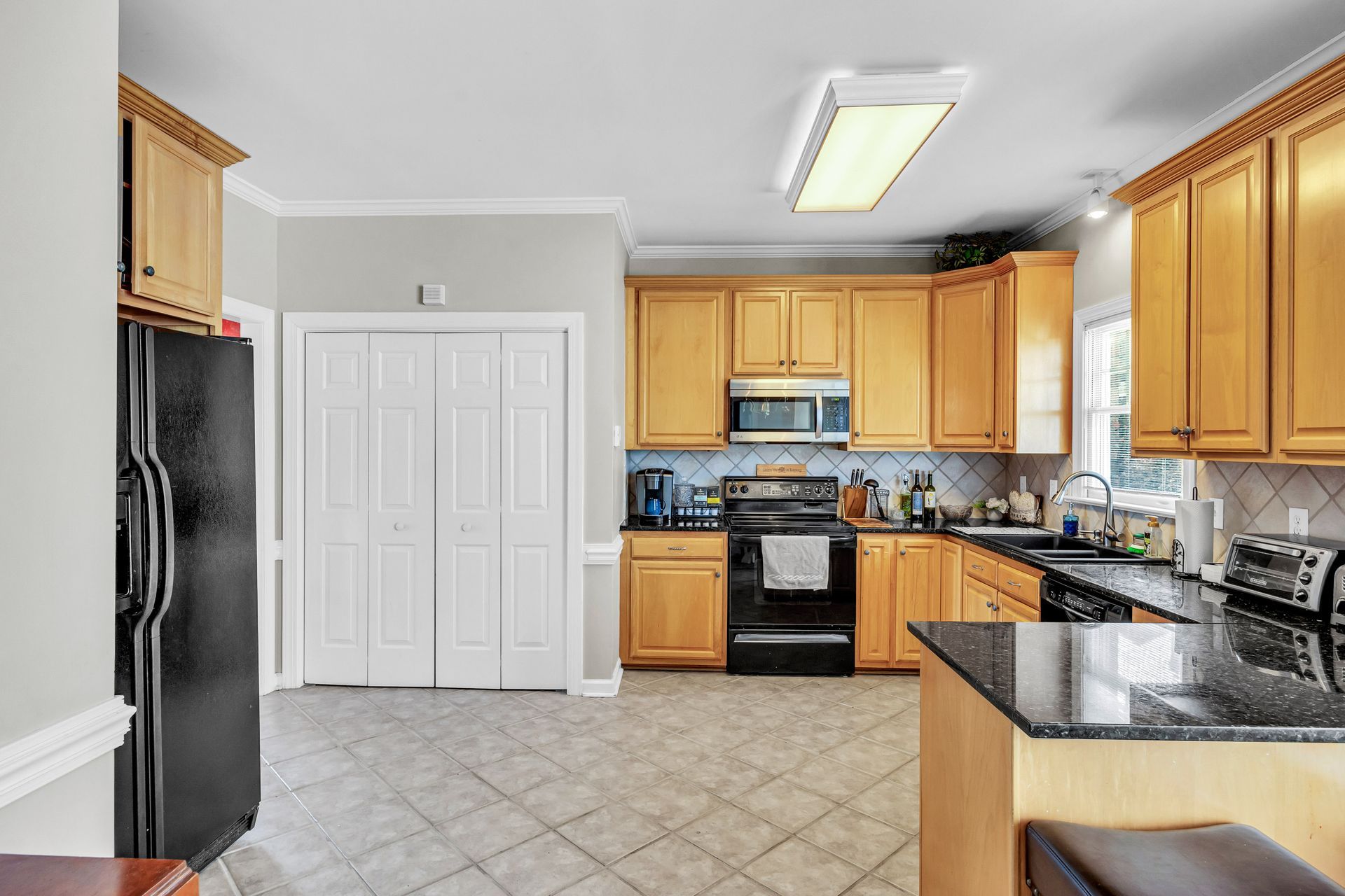 Bright kitchen with wood cabinets, black appliances, granite counters, and tiled floor