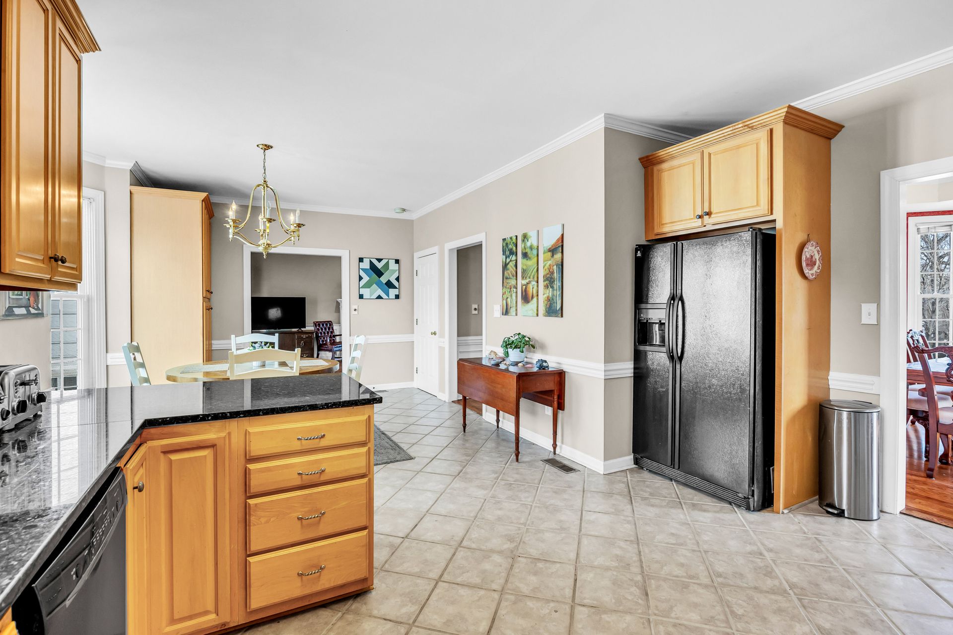 Bright kitchen with black appliances, wood cabinets, and tiled floor, opening to a dining area