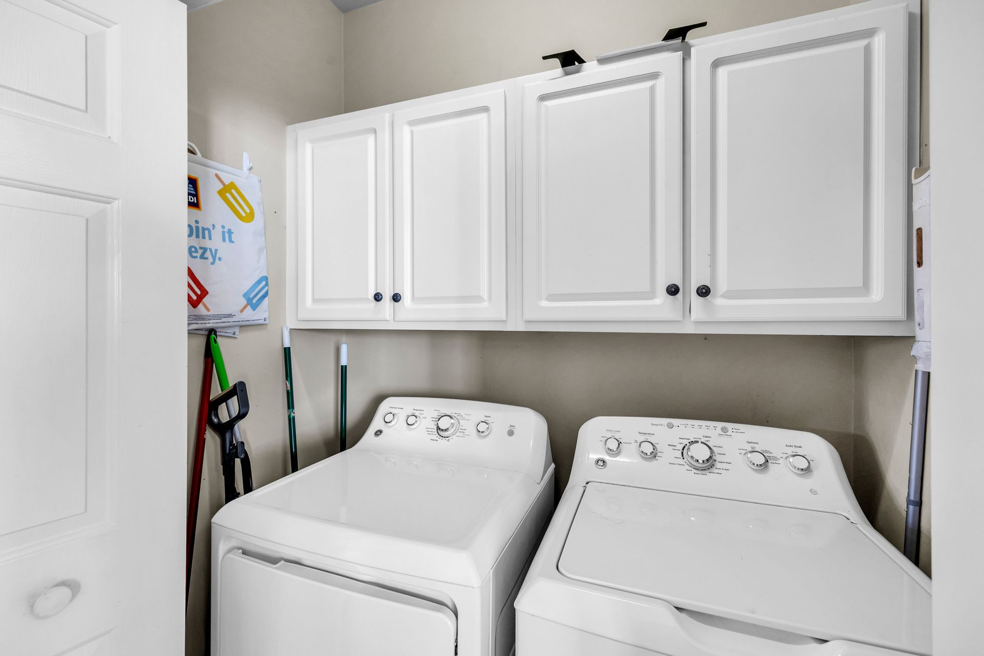 Laundry room with white washer and dryer under white cabinets and shelving