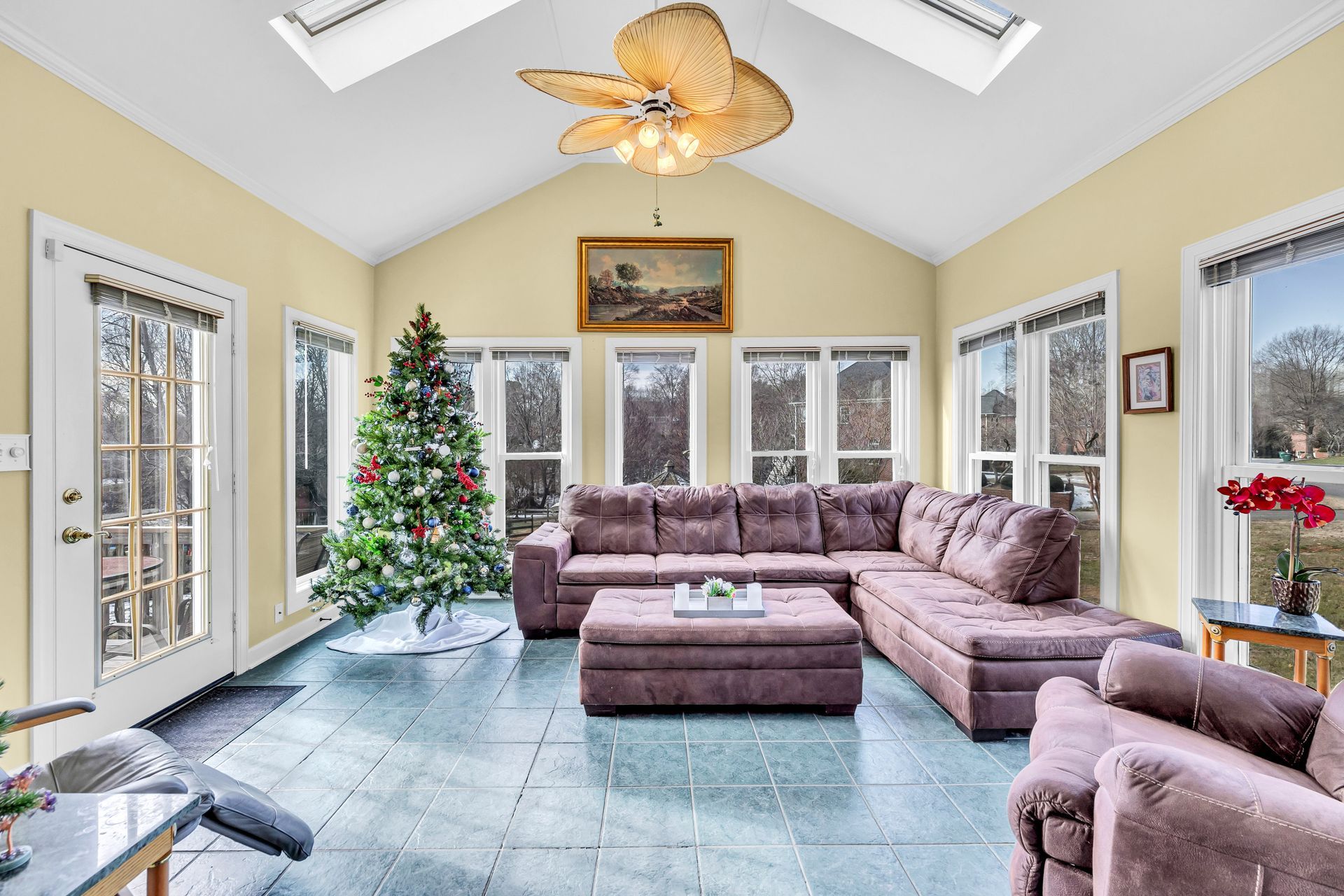 Bright sunroom with purple sectional, Christmas tree, tiled floor, and large windows