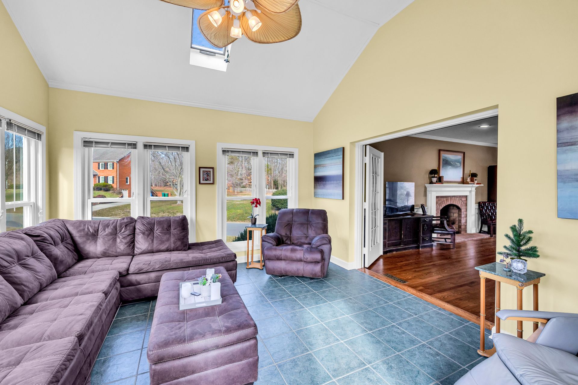 Bright living room with purple sectional, blue rug, bay windows, and hardwood dining area beyond the archway