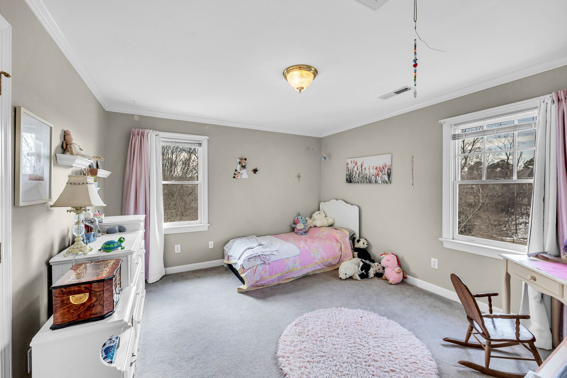 Bright bedroom with twin beds, gray walls, windows, and a rocking chair on the right.