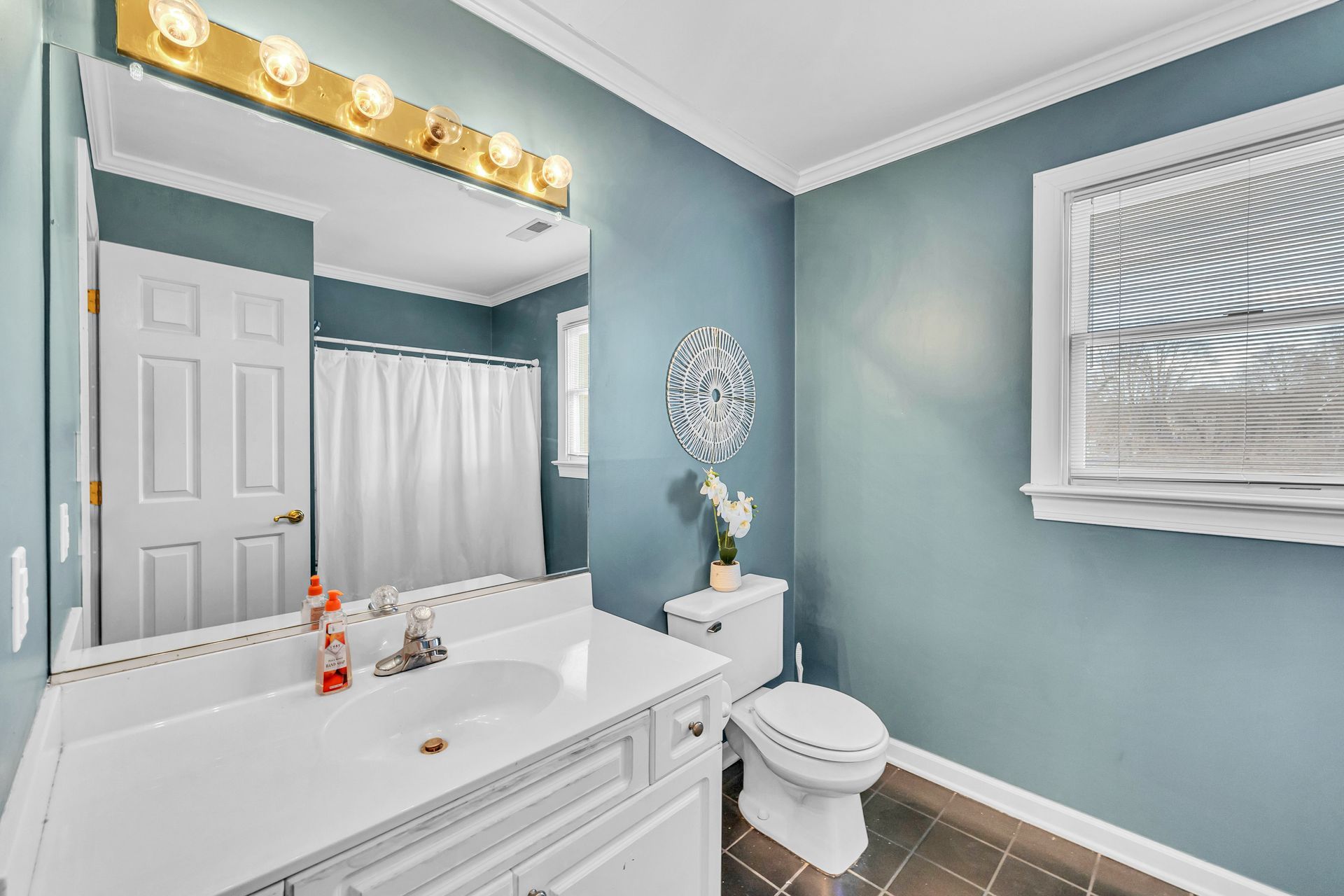 Bright blue bathroom with white vanity, large mirror, toilet, and tiled floor