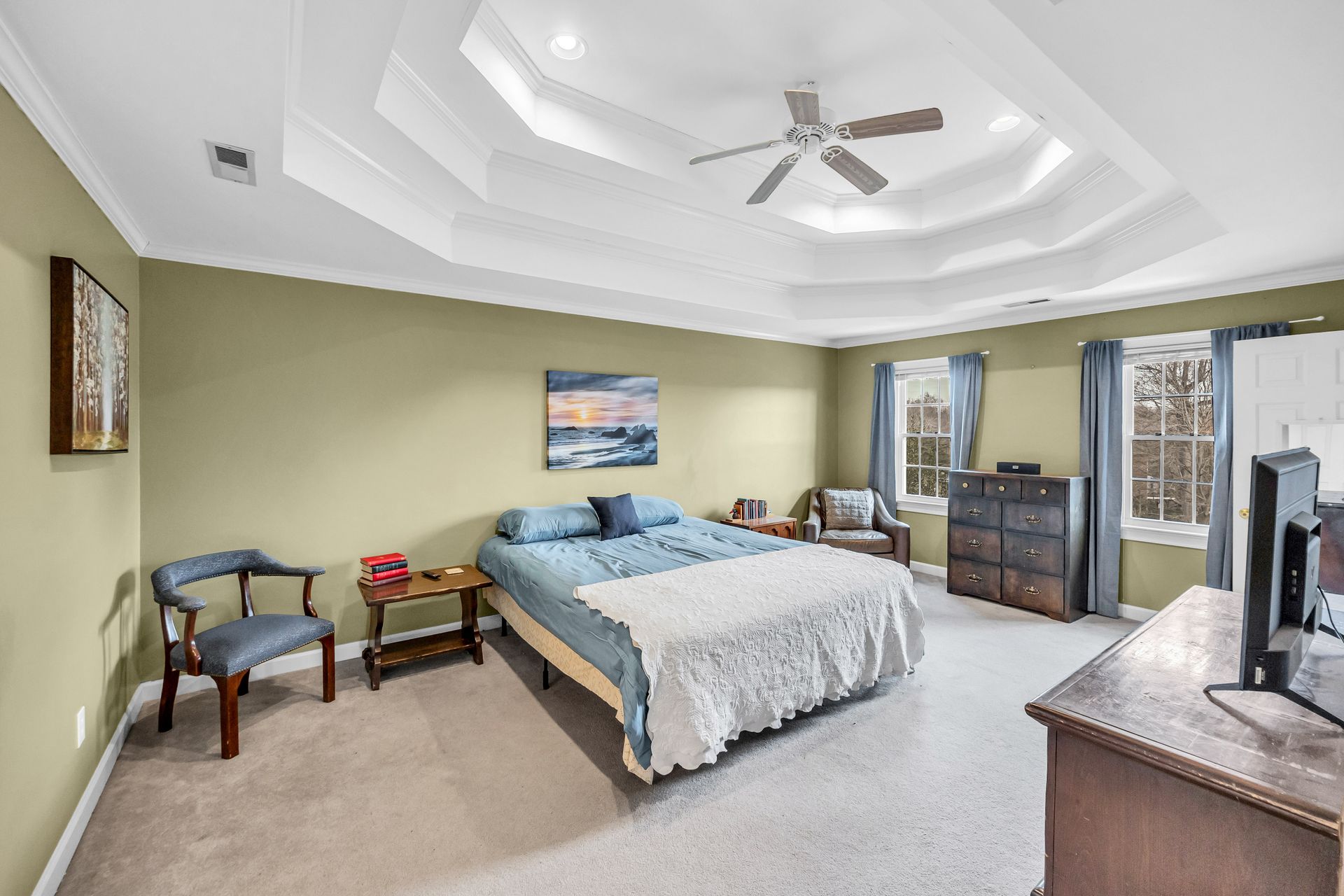 Spacious bedroom with a bed, dresser, ceiling fan, and soft green walls