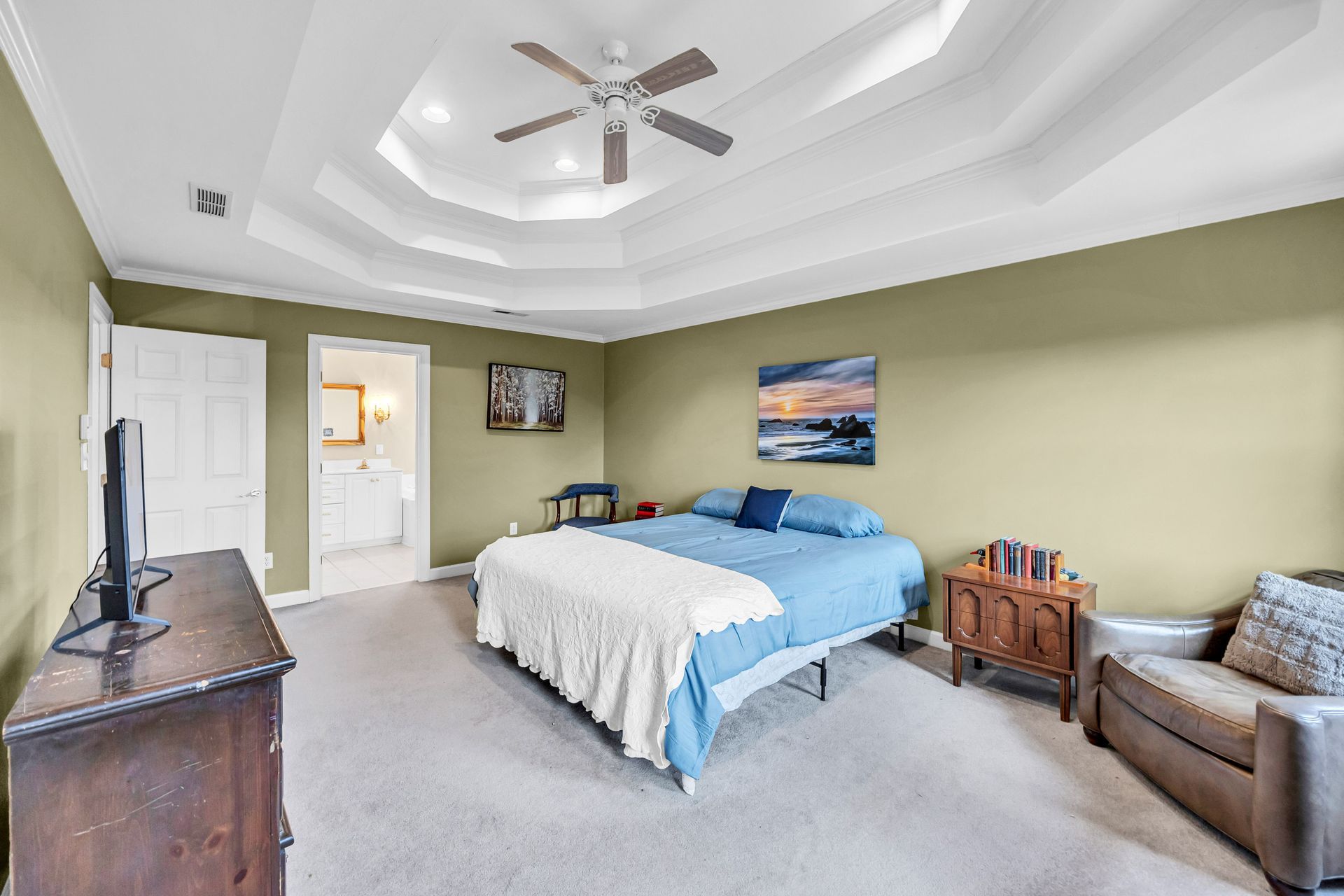 Bedroom with a blue bed, olive walls, ceiling fan, dresser, chair, and wall art
