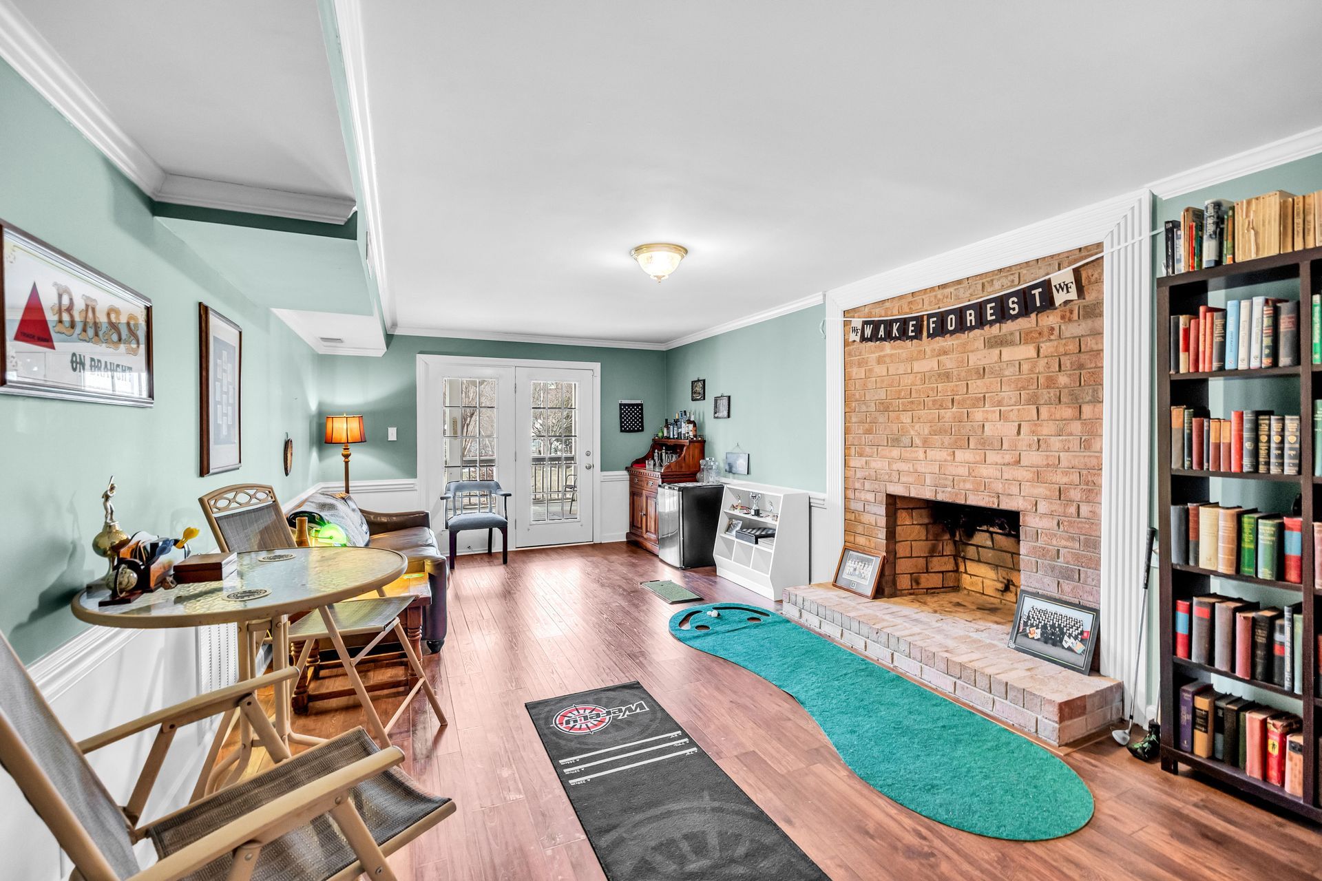 Bright dining room with teal walls, brick fireplace, bookshelves, and a long table by a large window