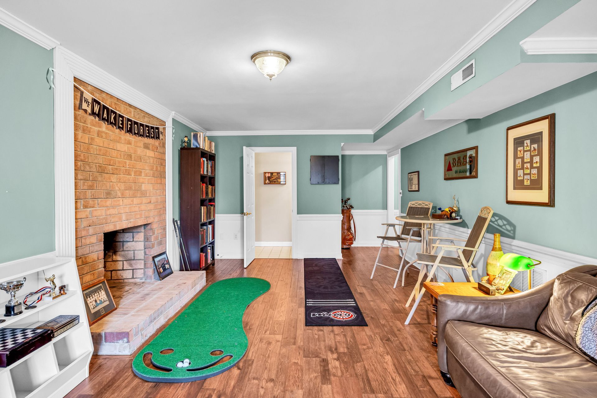 Long living room with mint walls, wood floor, leather chair, sofa, chairs, and a fireplace area