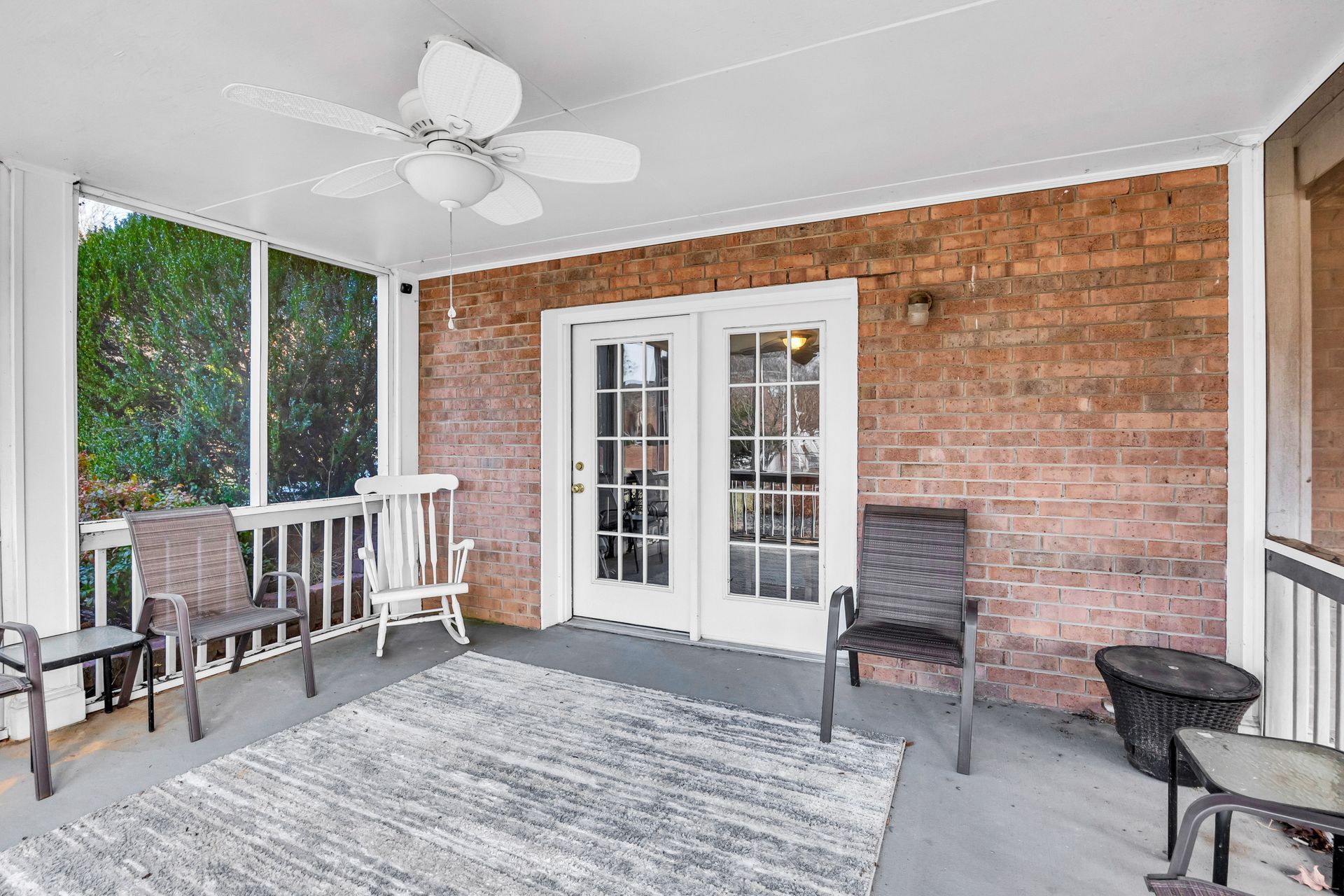 Covered patio with white ceiling fan, wicker chairs, brick wall, and double French doors