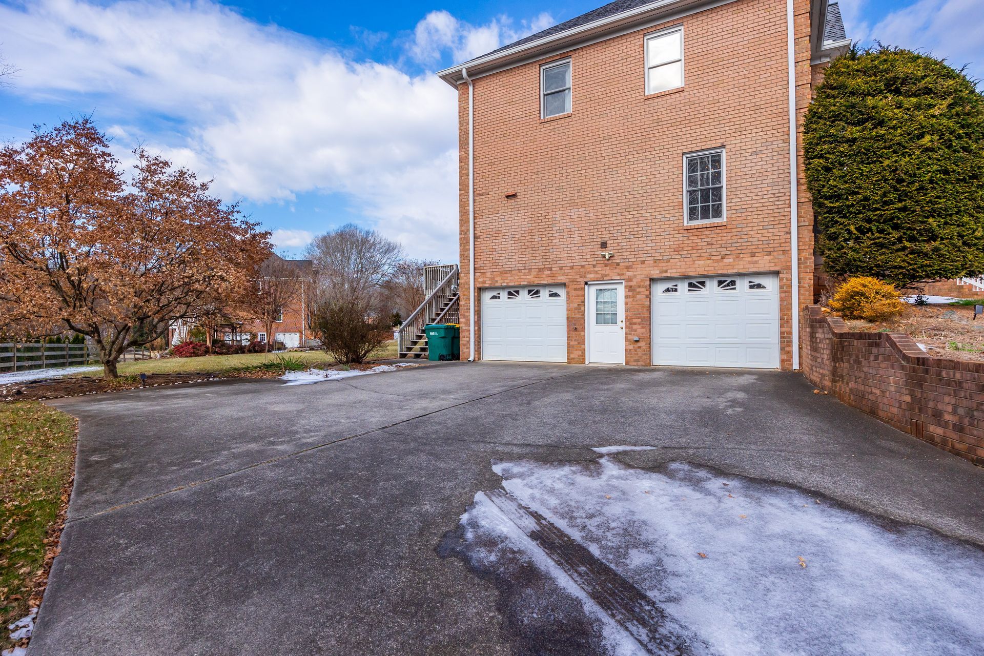 Brick townhouse with two white garage doors and a wet driveway on a cloudy day