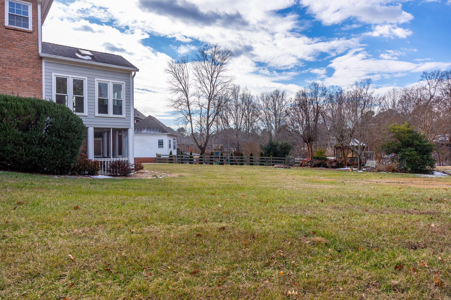 Suburban house beside a wide grassy yard under a partly cloudy sky
