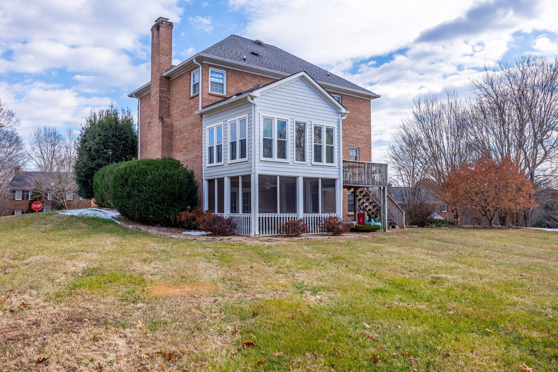 Two-story brick house with white screened porch on a grassy lot under a cloudy sky