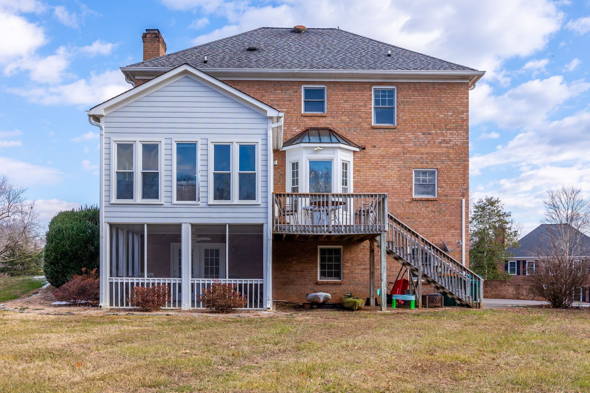 Two-story brick house with white porch, balcony, and exterior stairs on a grassy lot
