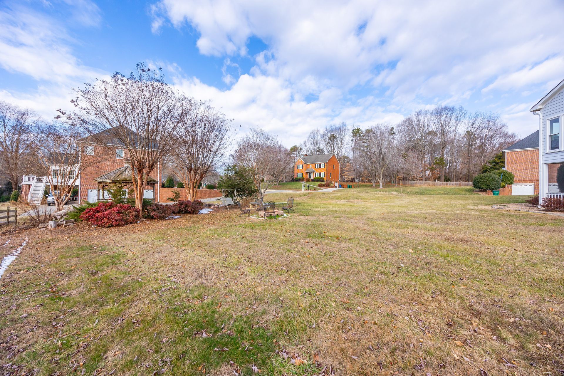 Open grassy lot beside brick townhomes under a cloudy blue sky.
