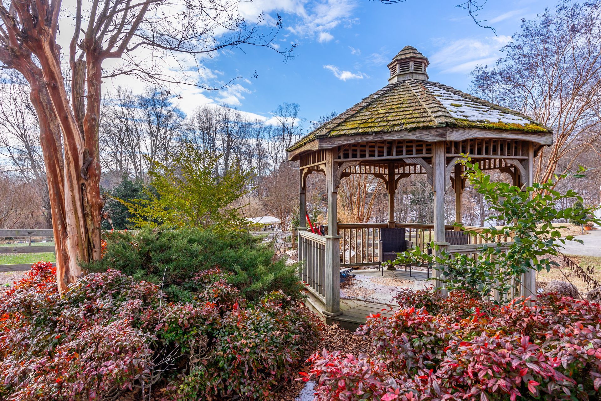 Gazebo in a colorful garden with pink shrubs, trees, and a lake in the background