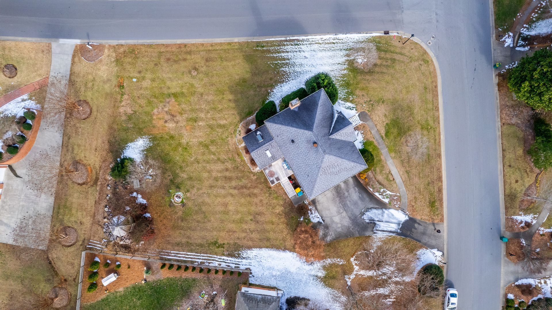 Aerial view of a house with a gray roof beside a road and large grassy yard in a suburban neighborhood