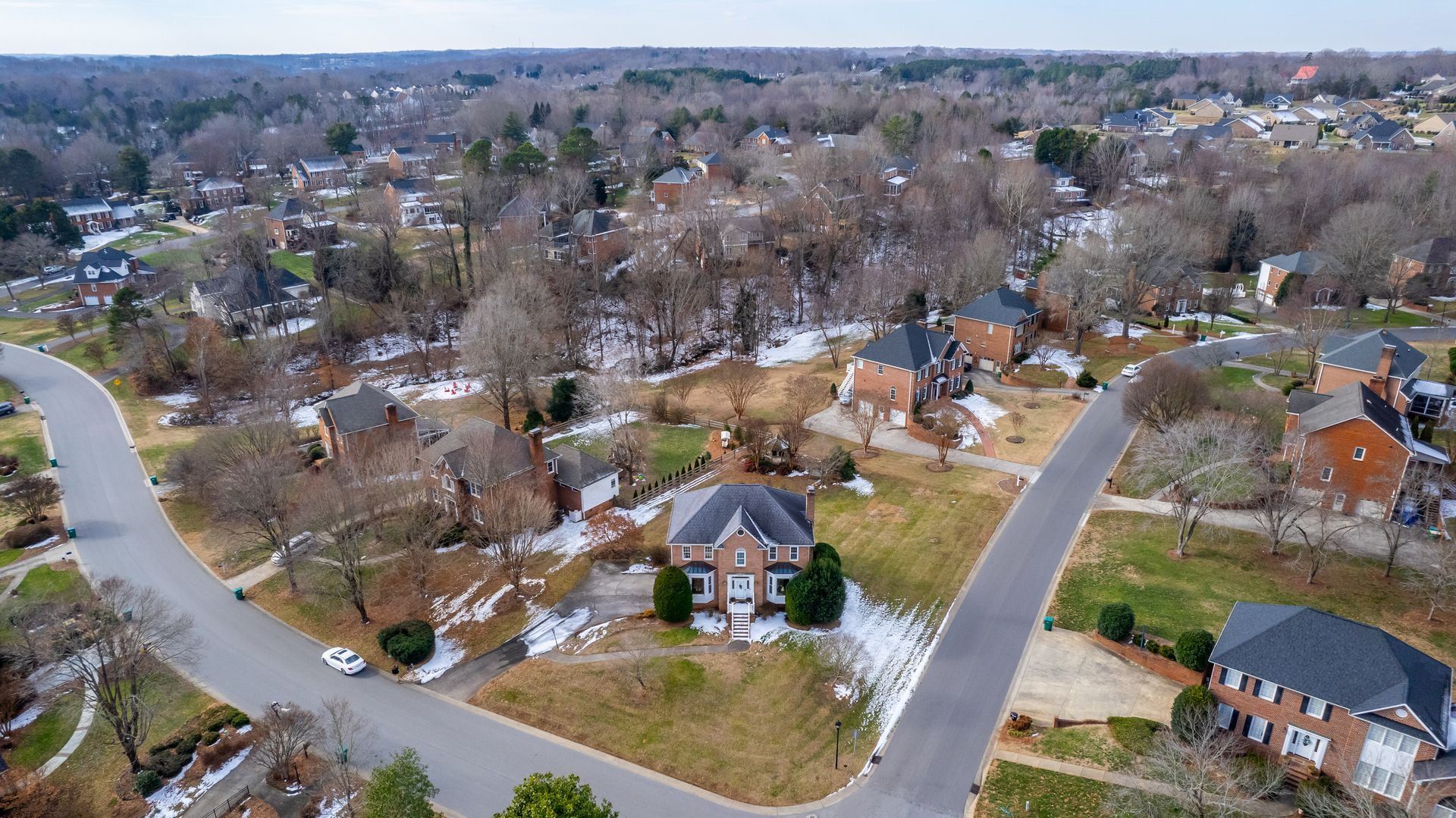 Aerial view of a suburban neighborhood with houses, roads, and bare winter trees.
