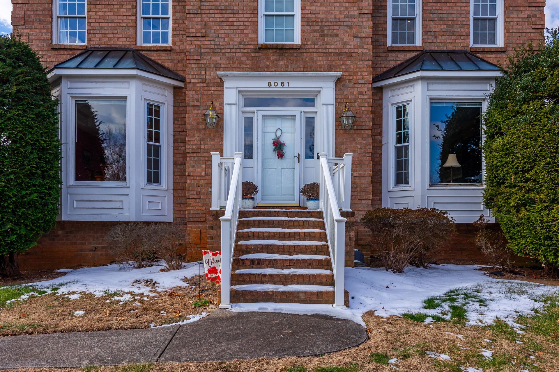 Front entrance of a brick townhouse with white trim, steps, and snow on the ground.