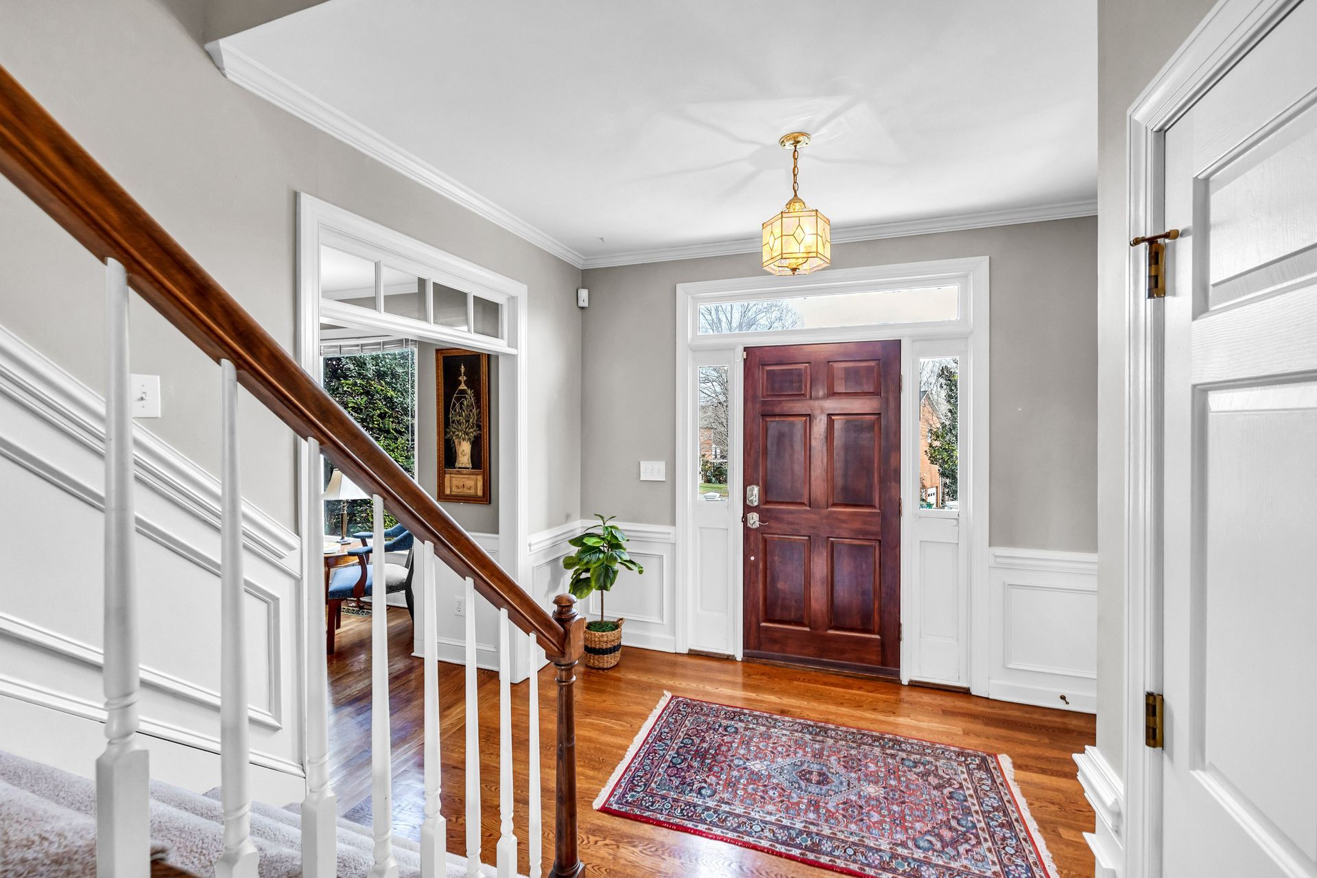 Bright entry hall with staircase, wood front door, white trim, and patterned rug.