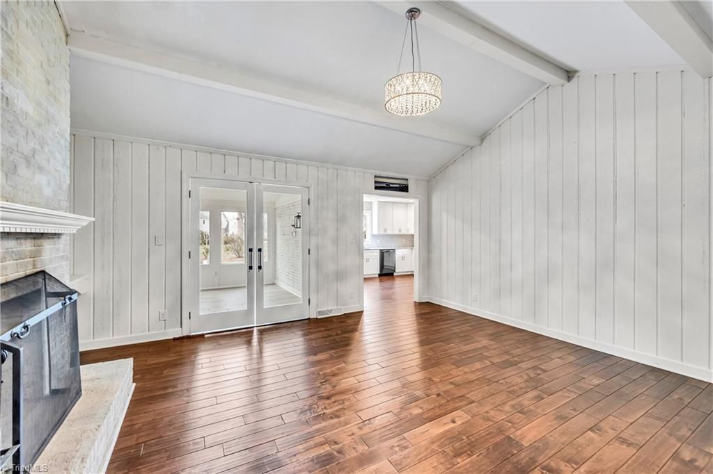 Empty white-paneled room with hardwood floor, chandelier, and fireplace