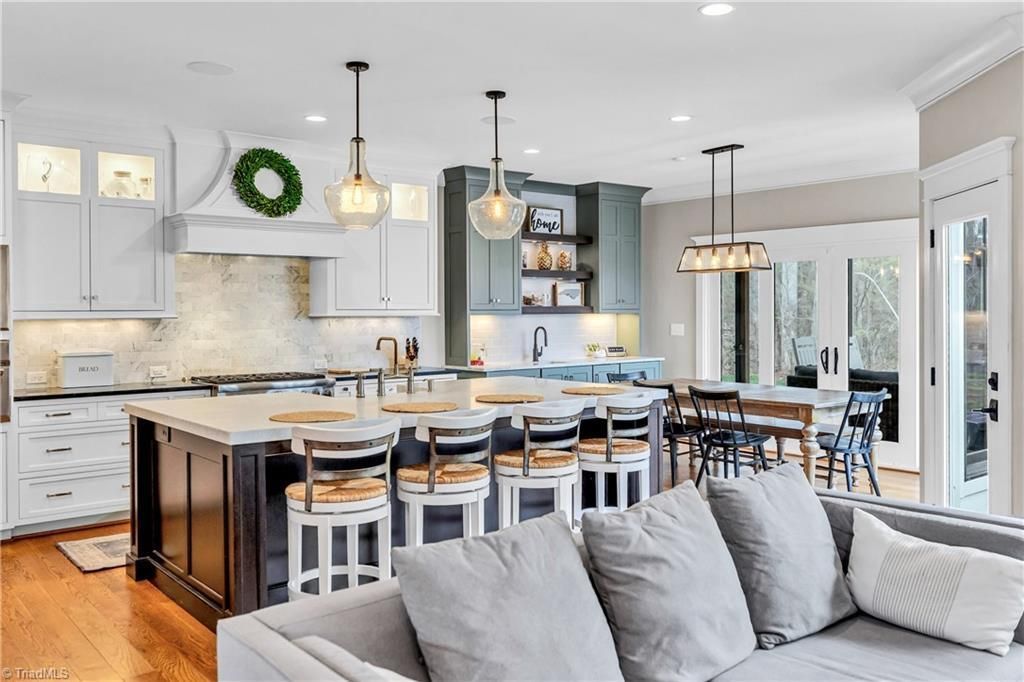 Bright open kitchen and dining area with island, gray sofa, white cabinets, and pendant lights