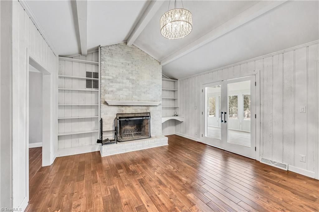 Bright living room with hardwood floors, white walls, a fireplace, staircase, and chandelier.