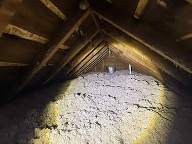 Attic interior with thick cellulose insulation. Wooden rafters and a vent pipe are visible.