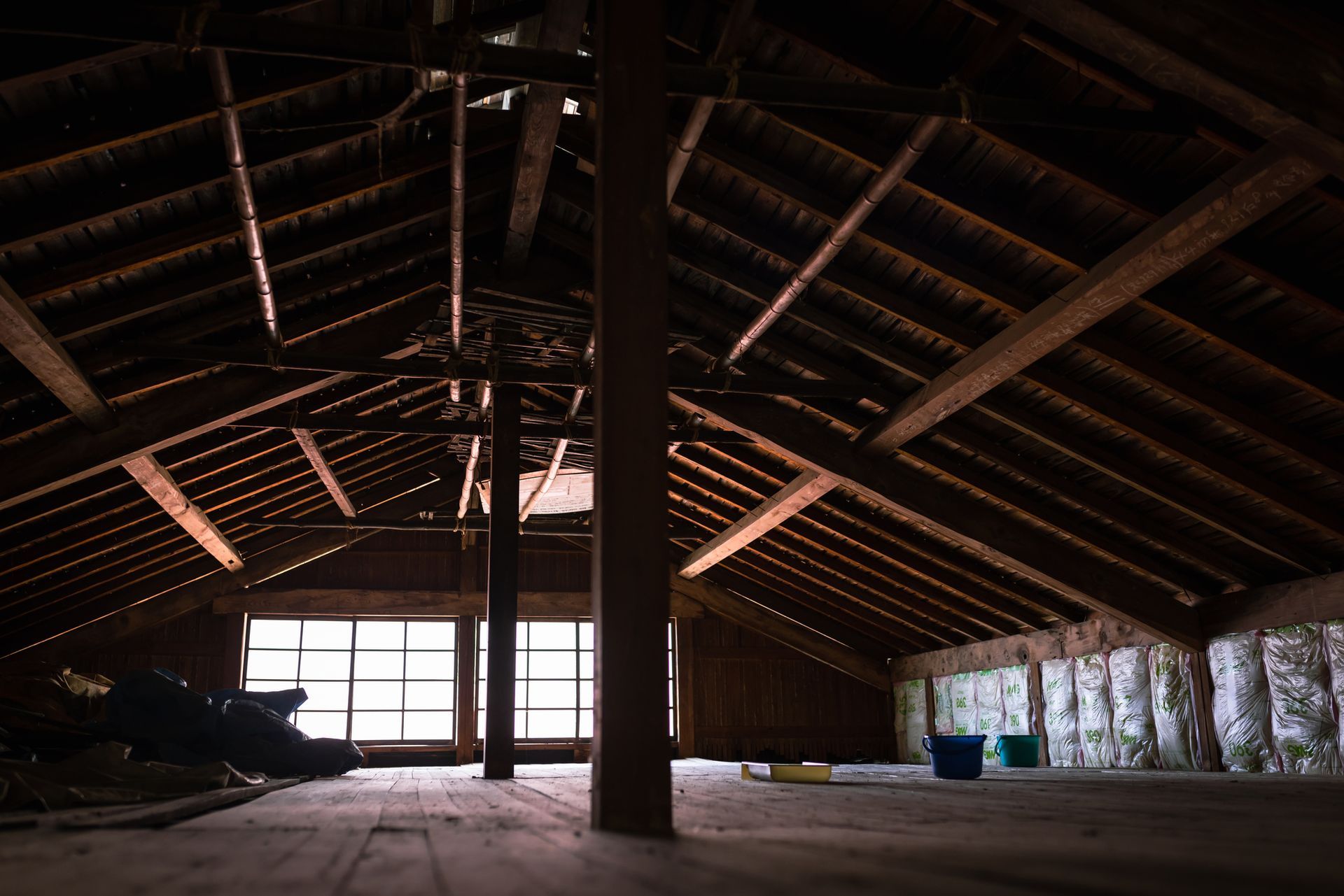 Person in protective suit spraying insulation into a wooden frame, inside a building.