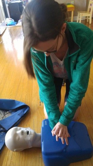 Woman performing CPR on a training dummy, pressing down with hands on chest; indoor setting.