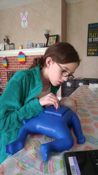 Girl with glasses examines a blue toy figure on a table, possibly for a medical game.