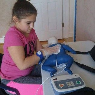 Girl practices CPR on a training dummy, applying a defibrillator. Indoors.