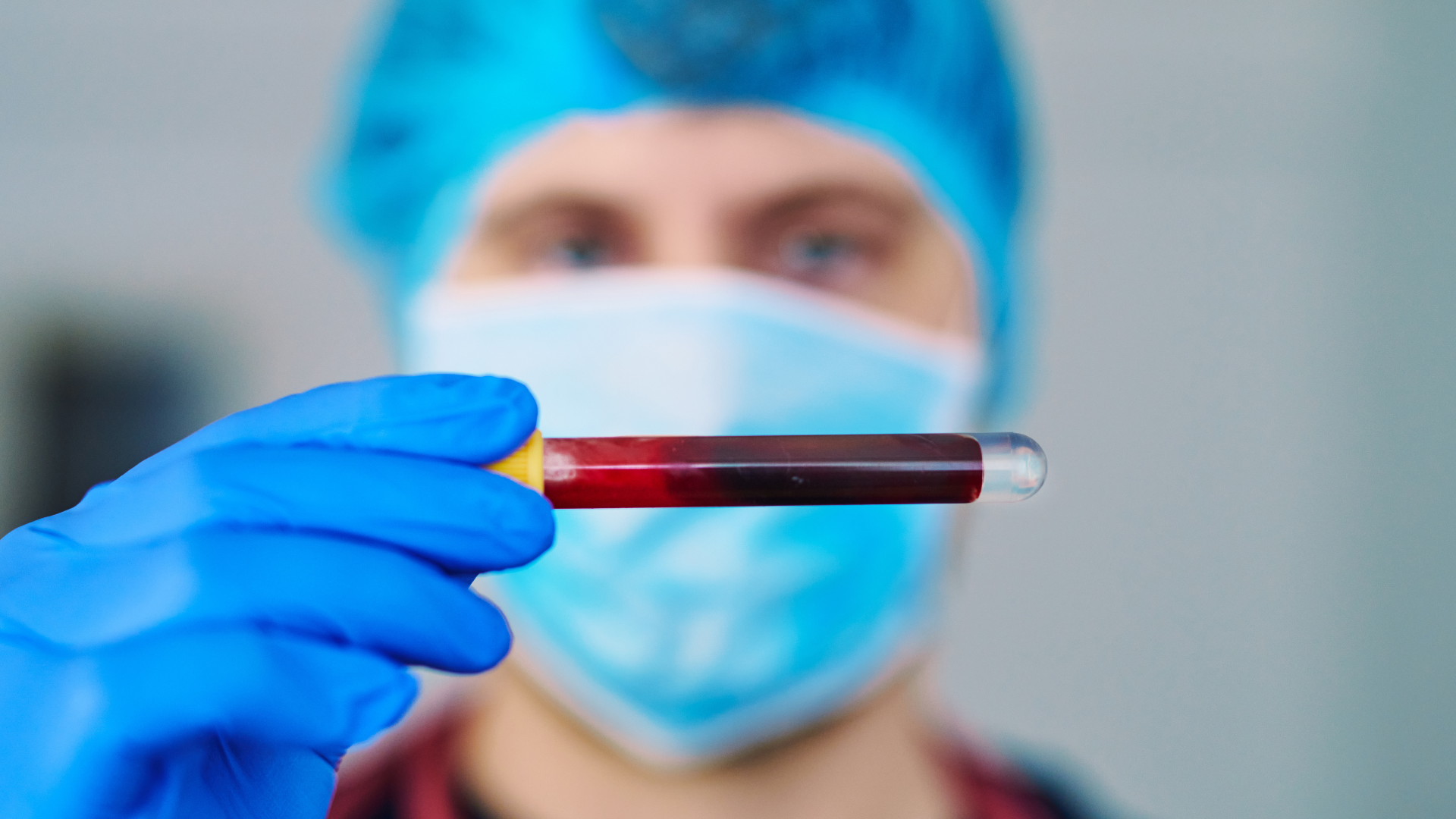 Person in medical attire holds a blood-filled test tube.
