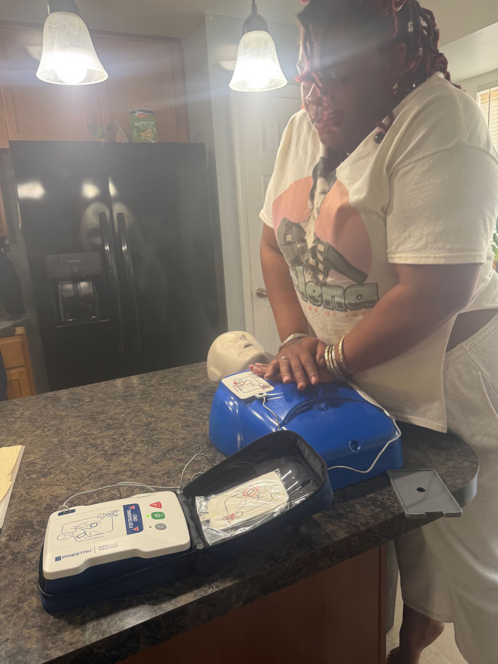 Person practicing CPR on a mannequin, with an open AED kit nearby on a counter.