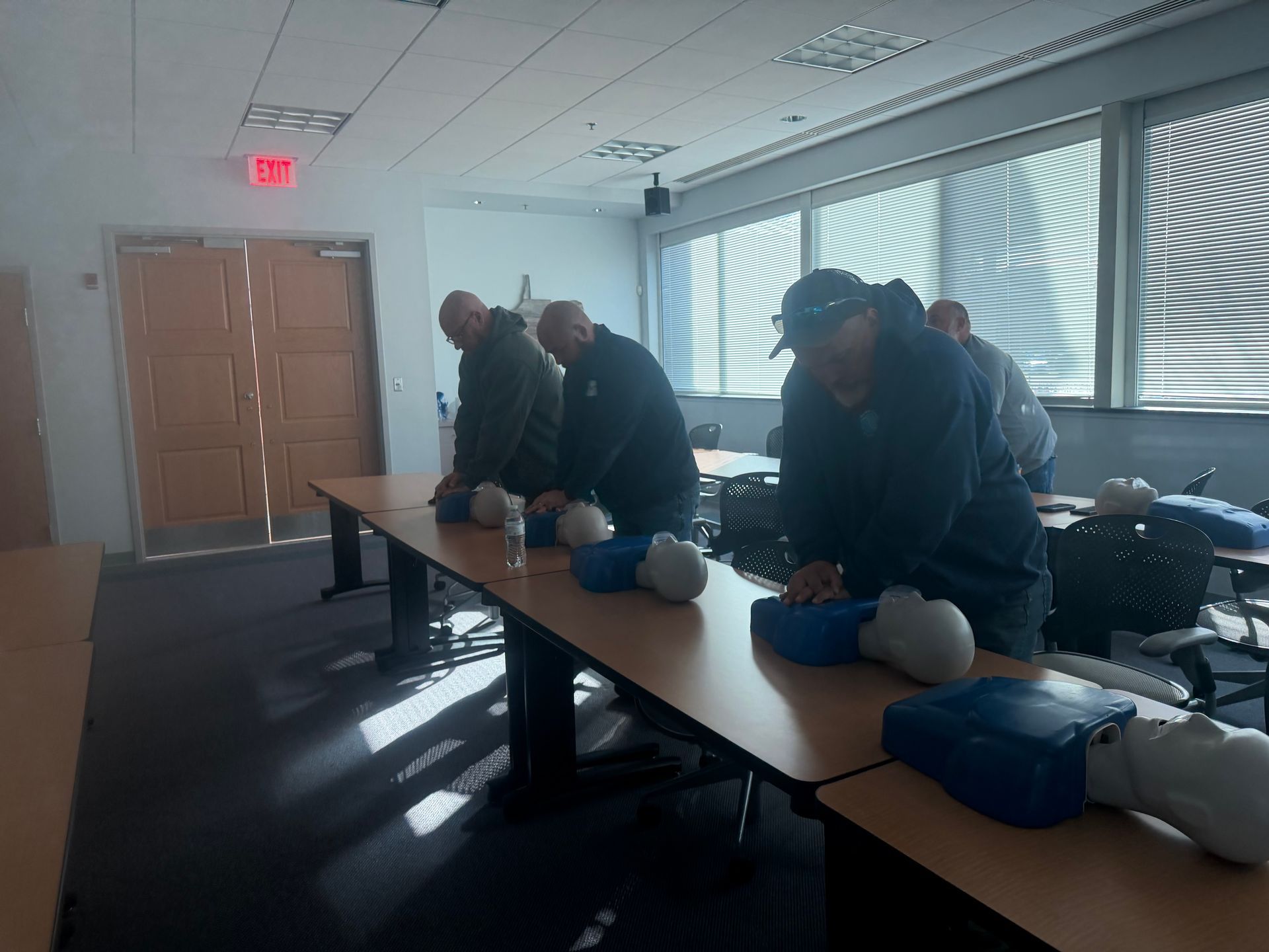 People practicing CPR on mannequins at a table in a classroom.
