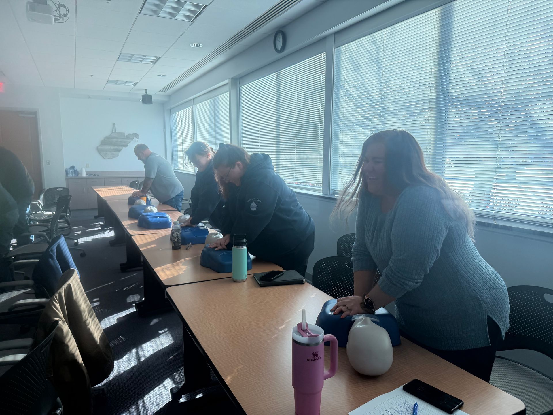 People practicing CPR on mannequins at a table in a classroom.