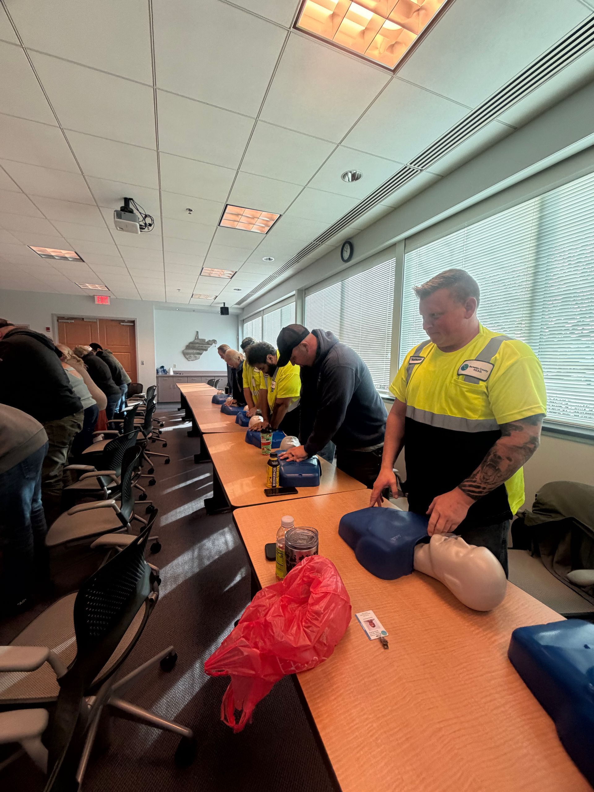 People in a classroom practicing CPR on mannequins.  Several people wear yellow safety vests.