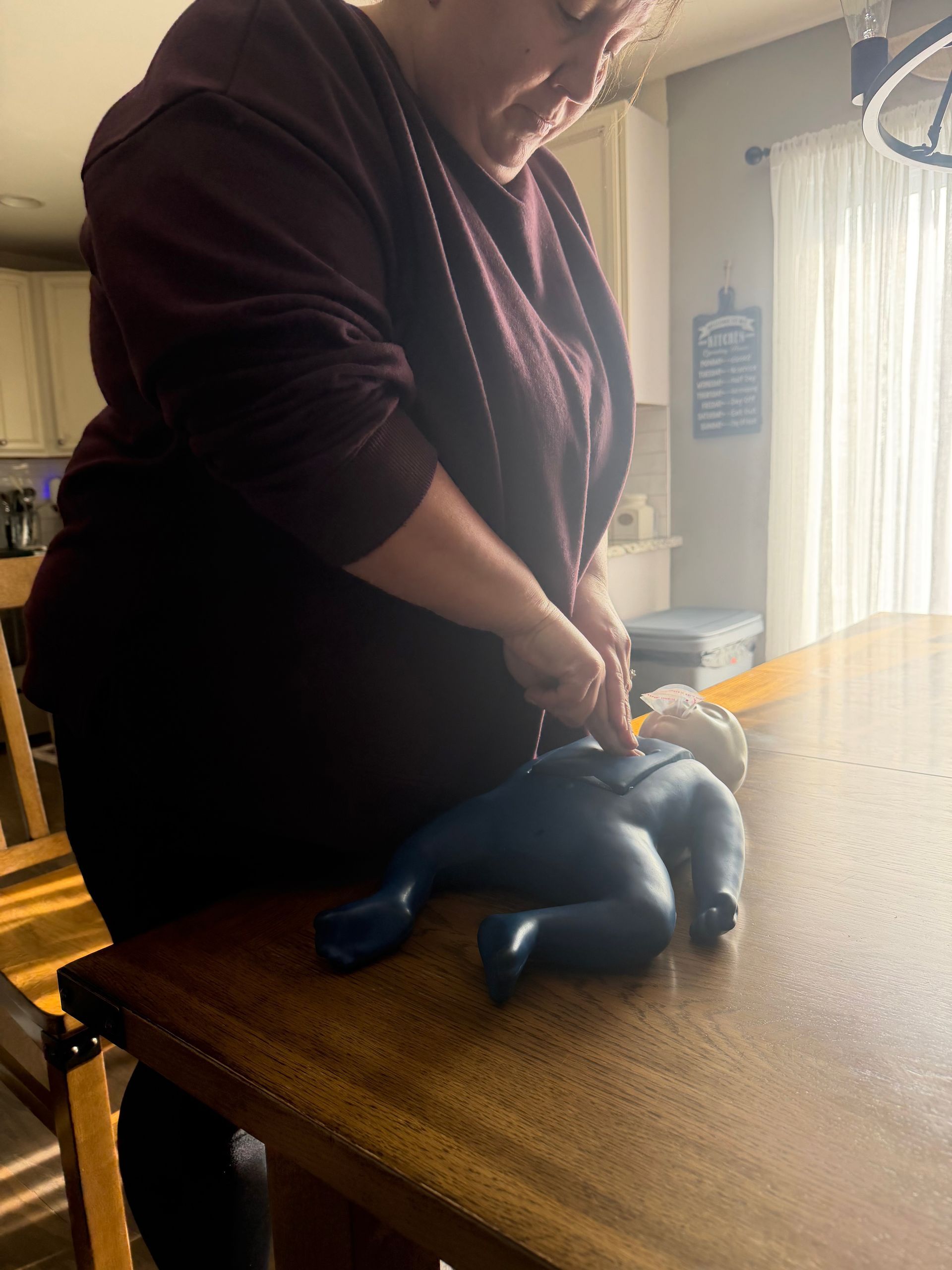Woman practicing CPR on a training doll, tabletop setting.