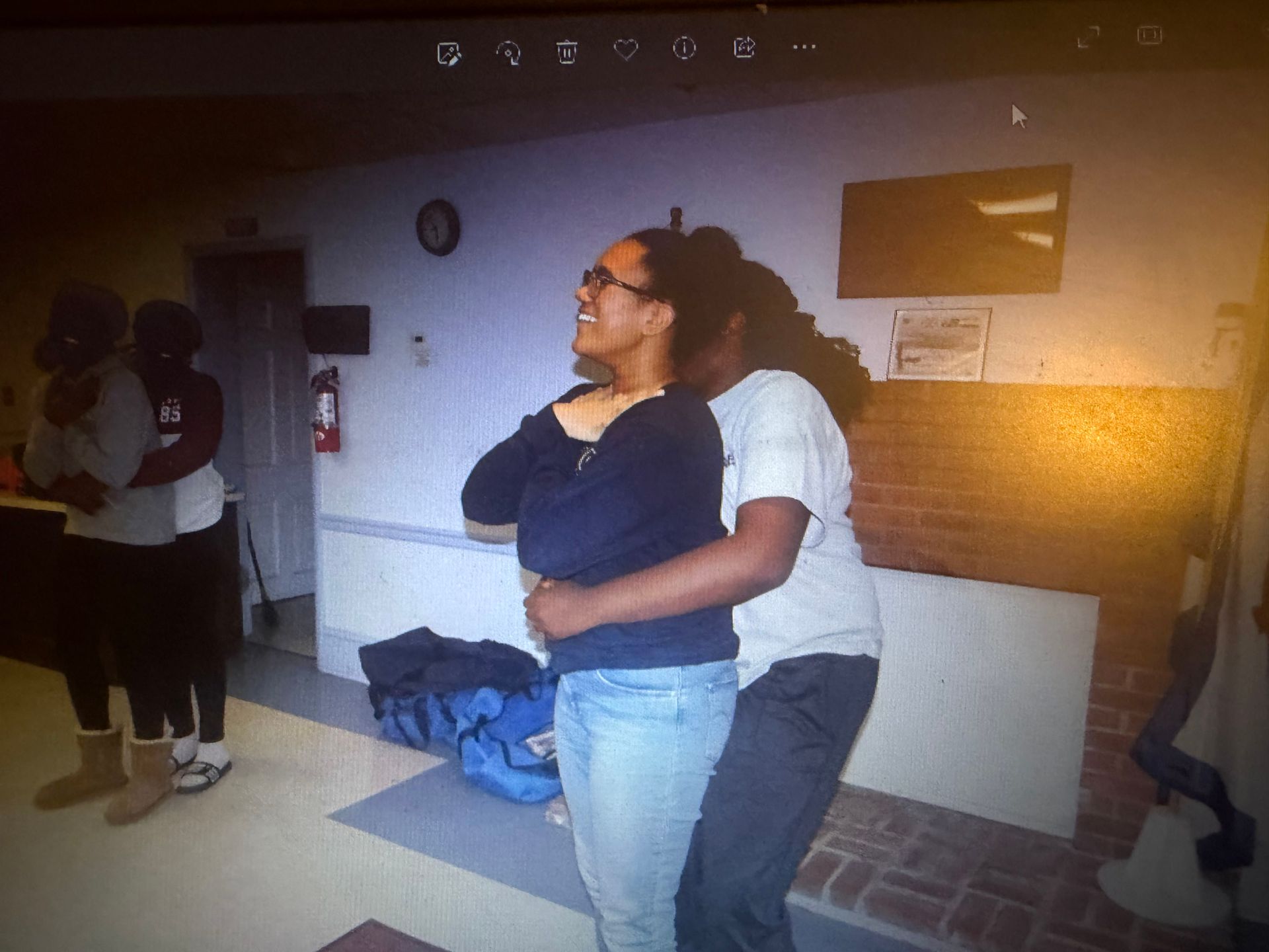 Three people hugging in a room. One woman smiles and is embraced. Two others hug near a door.