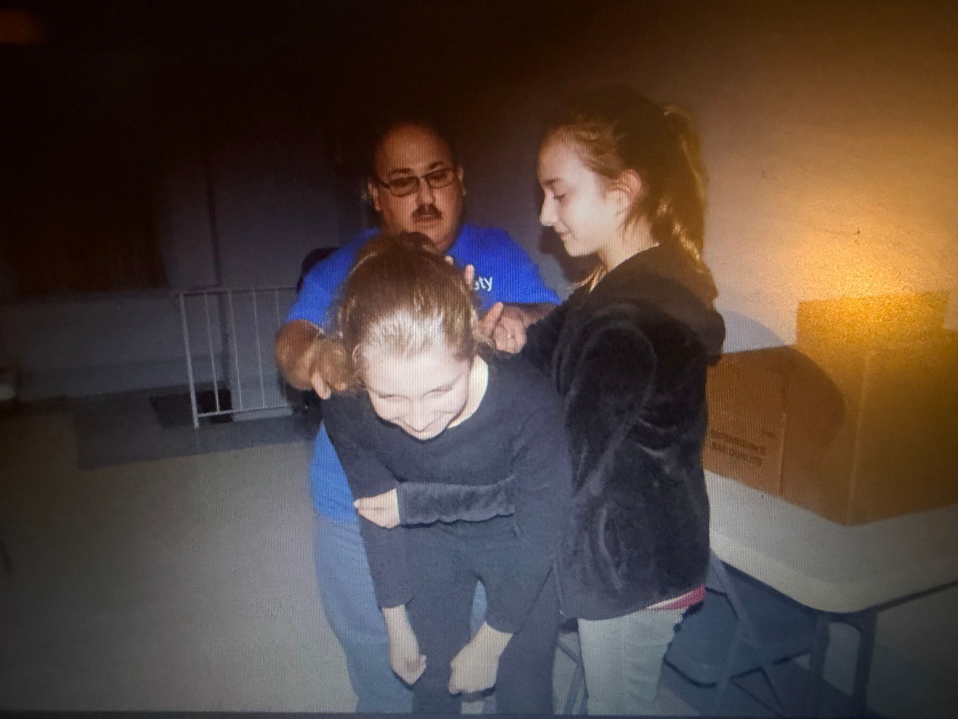 Man and young person assisting another young person. Person is hunched over. Inside.