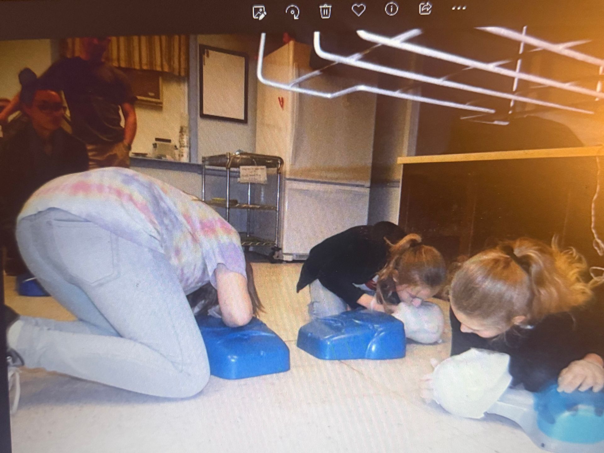 People kneeling, practicing CPR on blue training dummies indoors.