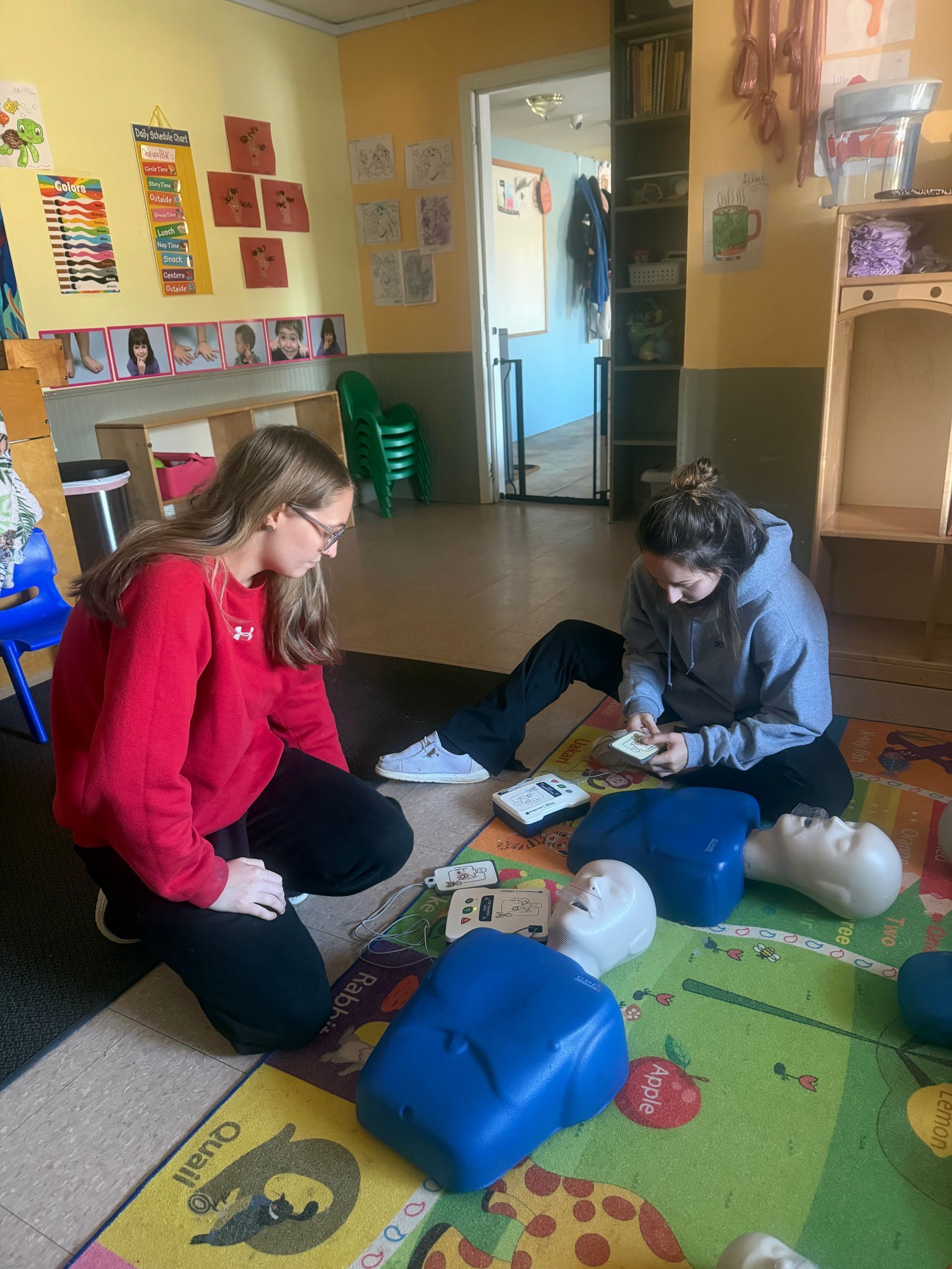 Two people practicing CPR on mannequins in a classroom.