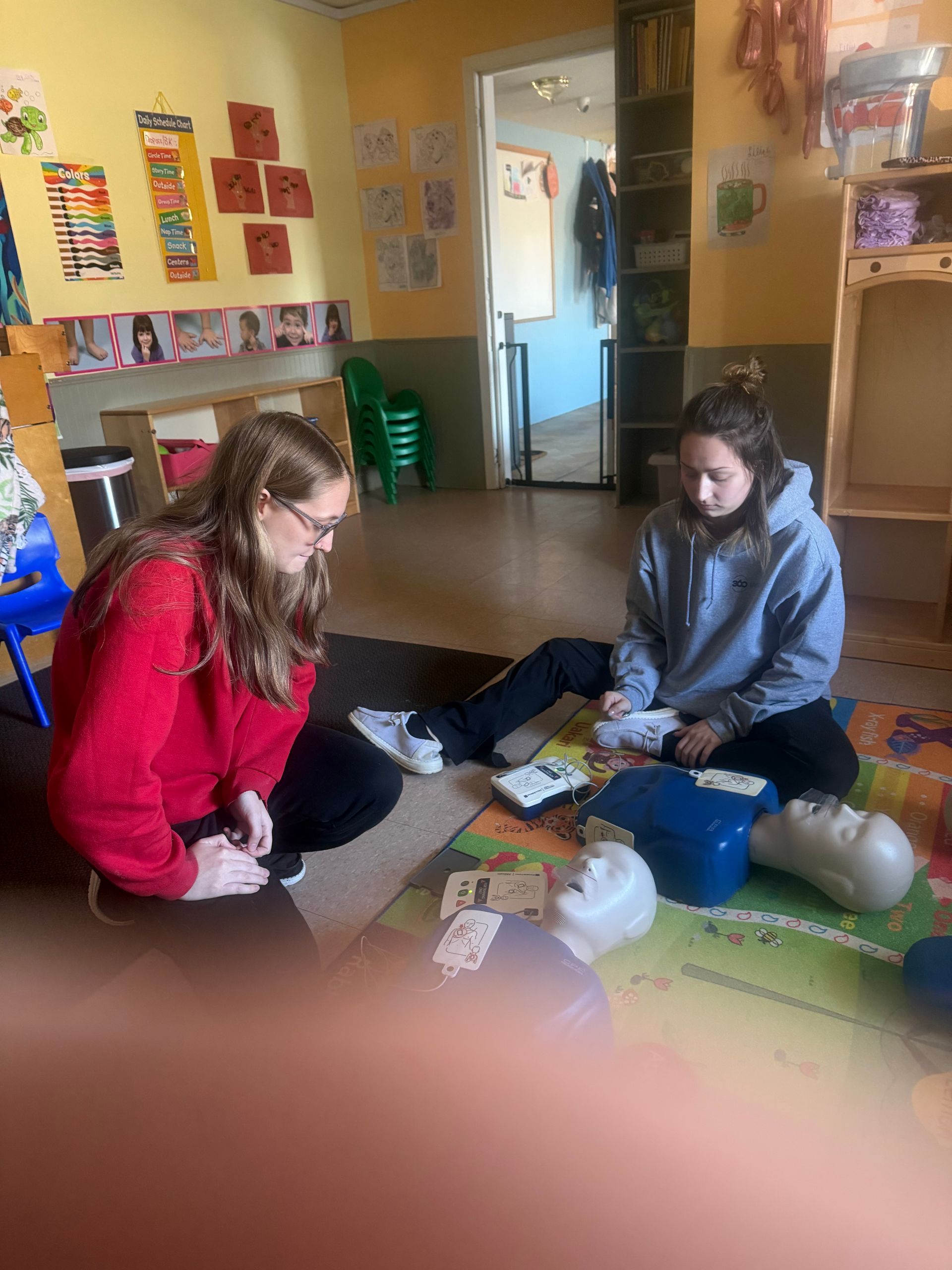 Two people practicing CPR on a training dummy in a classroom.