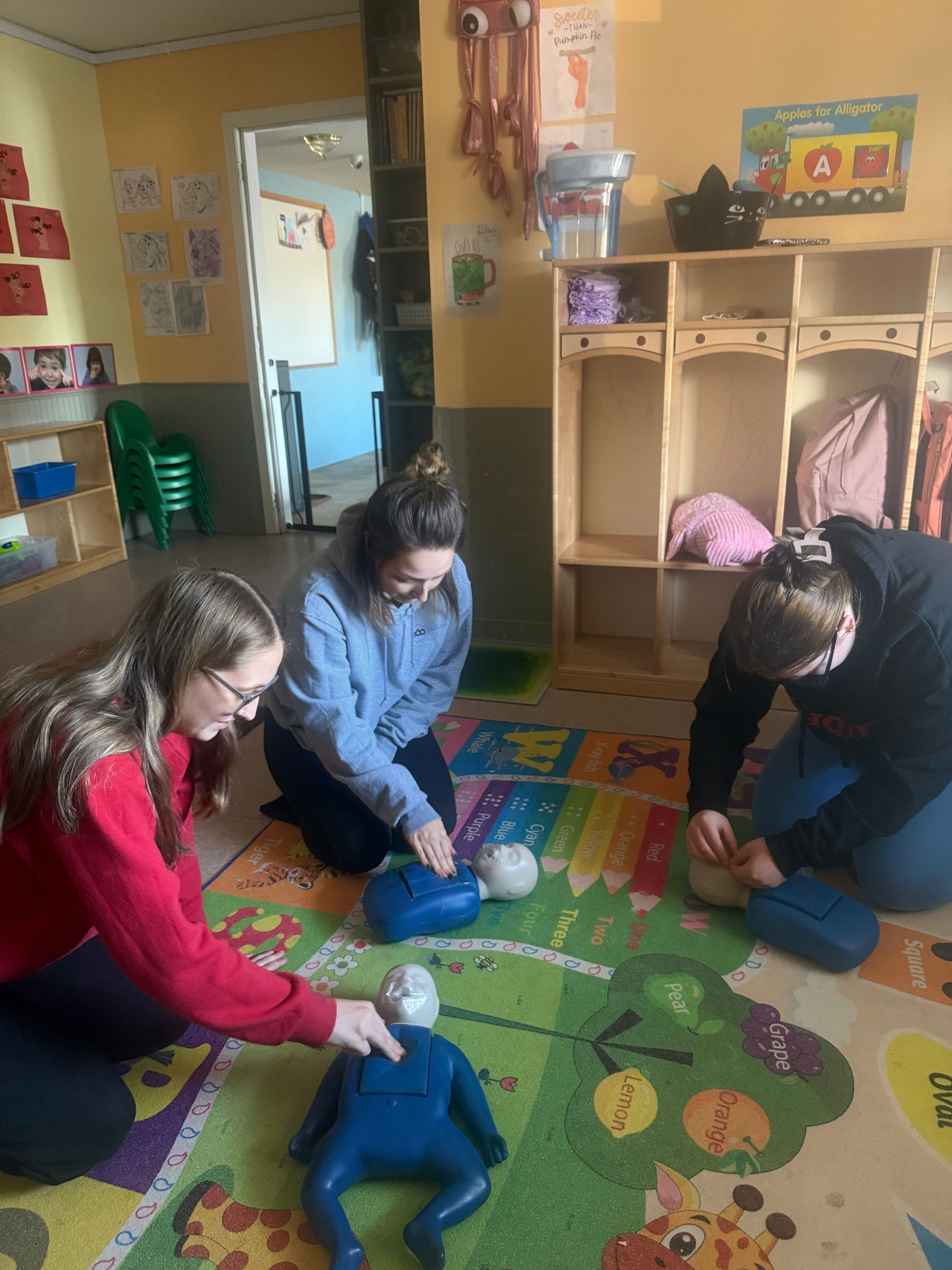 Three people practicing CPR on mannequins in a classroom.