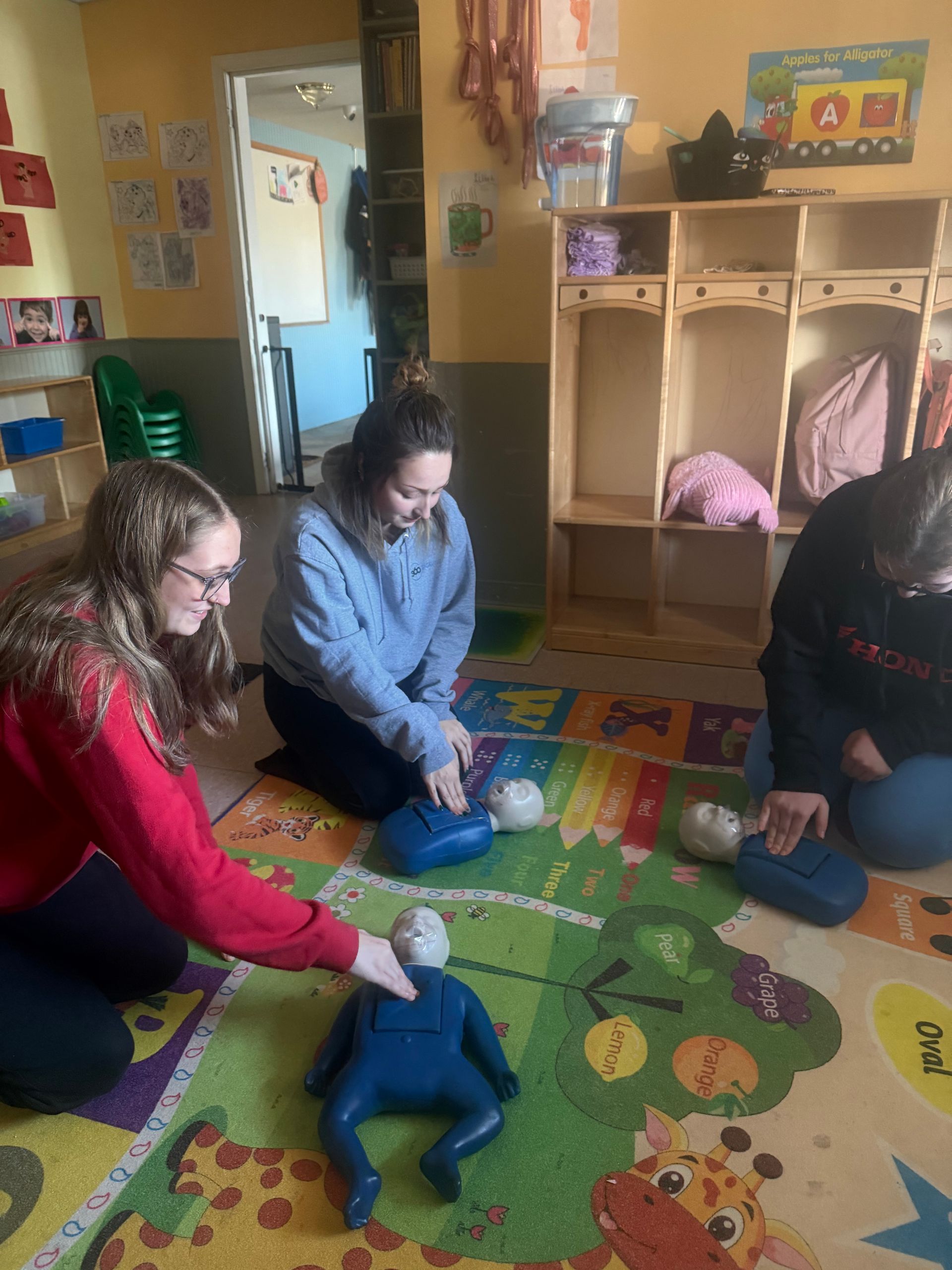Three people practice CPR on child-sized mannequins in a classroom.