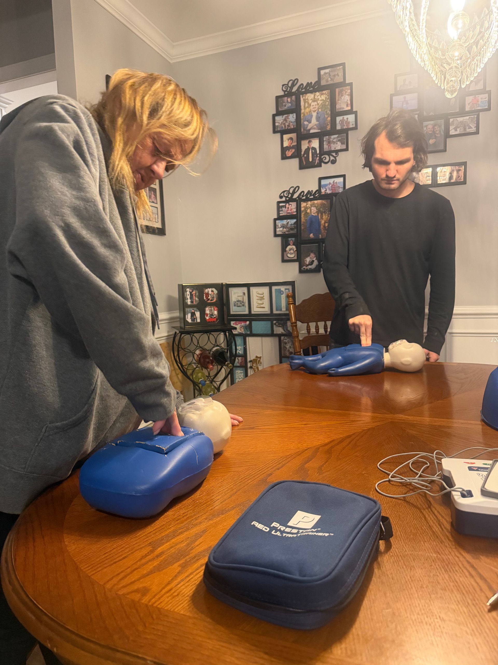 Two people practicing CPR on mannequins. They're in a room, using blue defibrillator trainers.