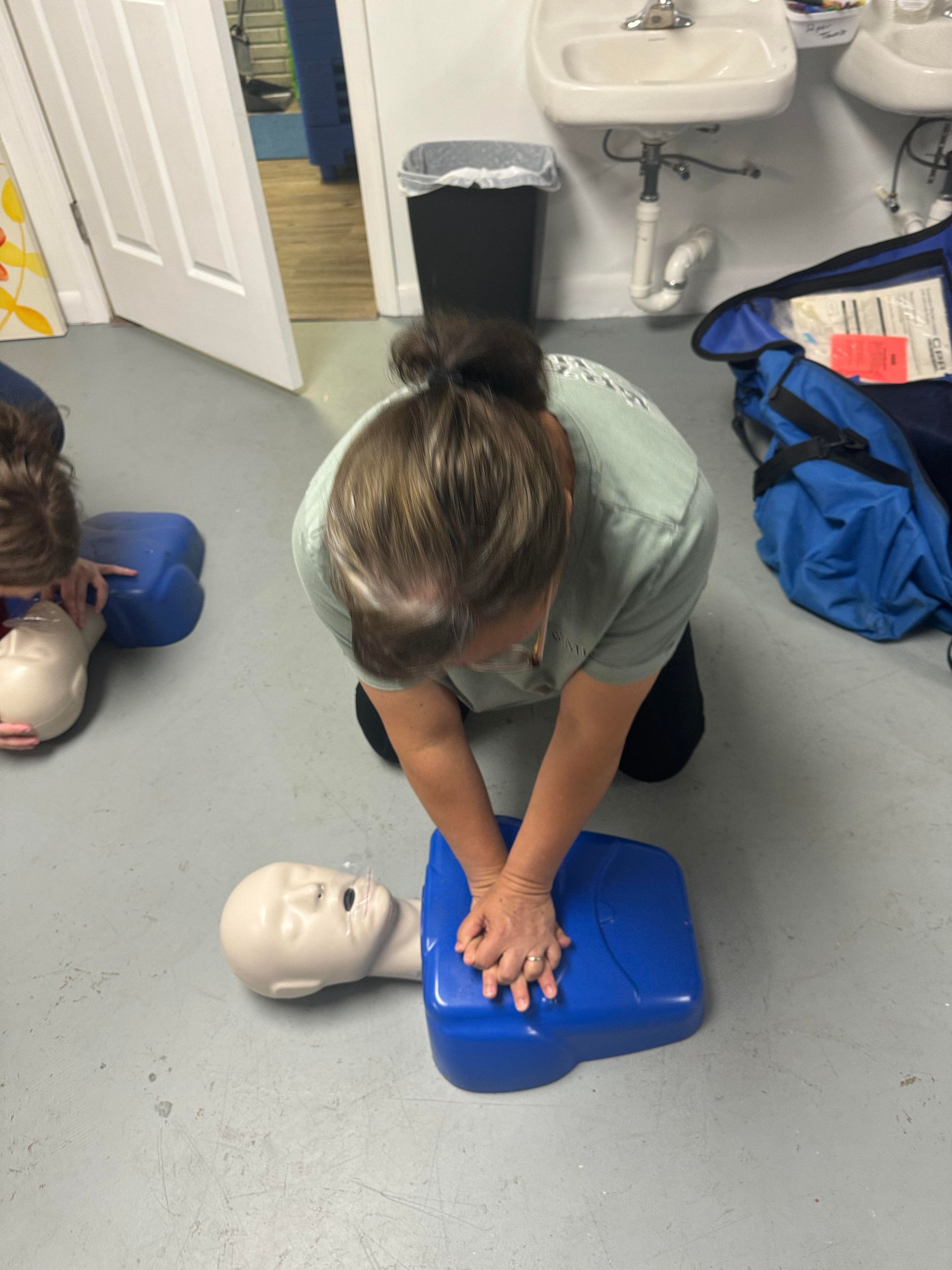 Woman performing CPR on a training dummy, indoors.