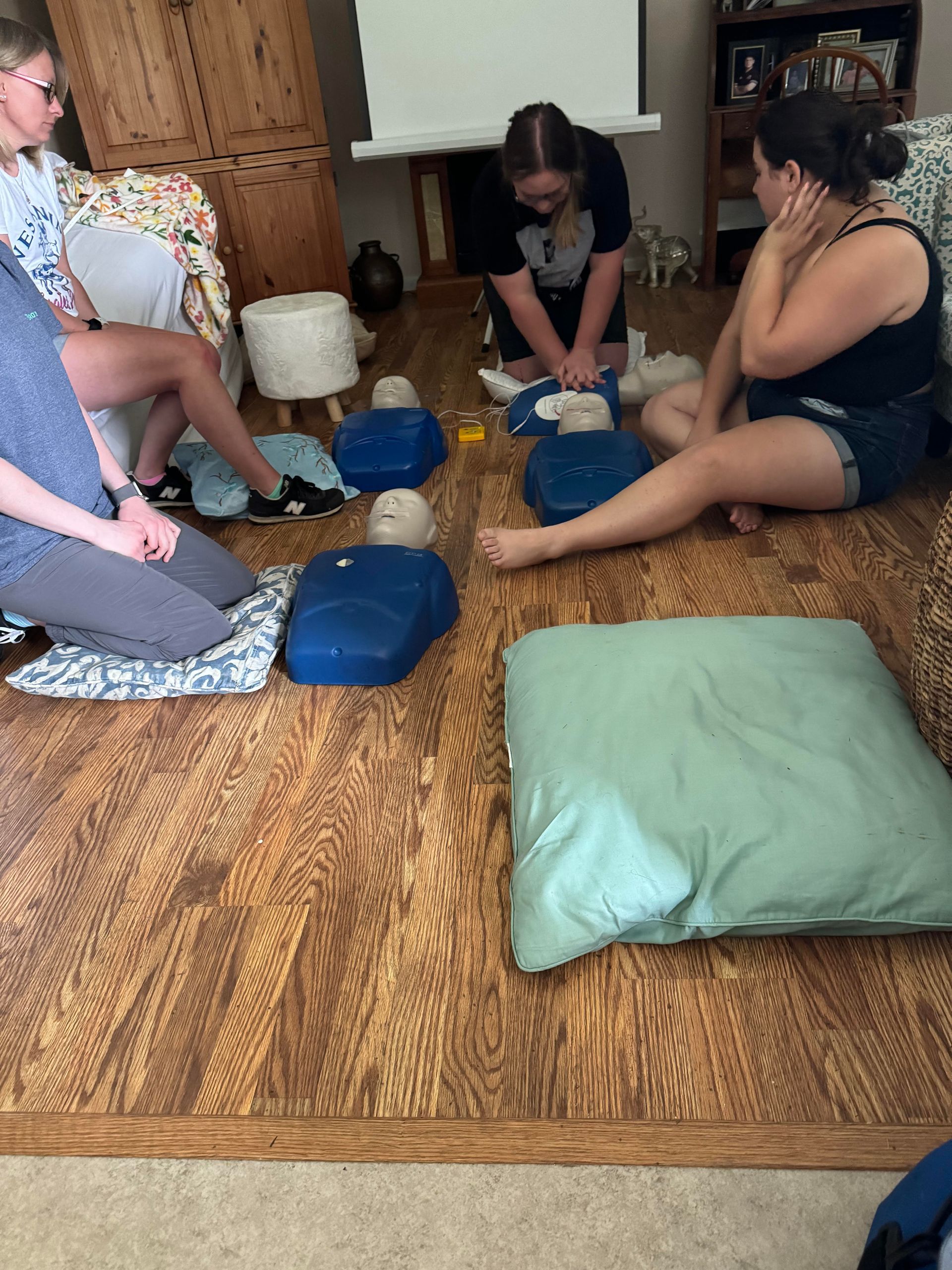 CPR class: People practicing compressions on mannequins on floor. Woman watches.